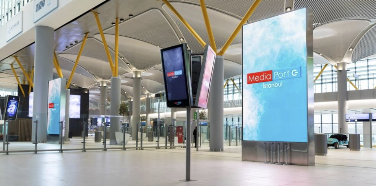Interior of Istanbul Airport featuring numerous digital signage screens displaying flight information, wayfinding and advertisements across a large terminal.